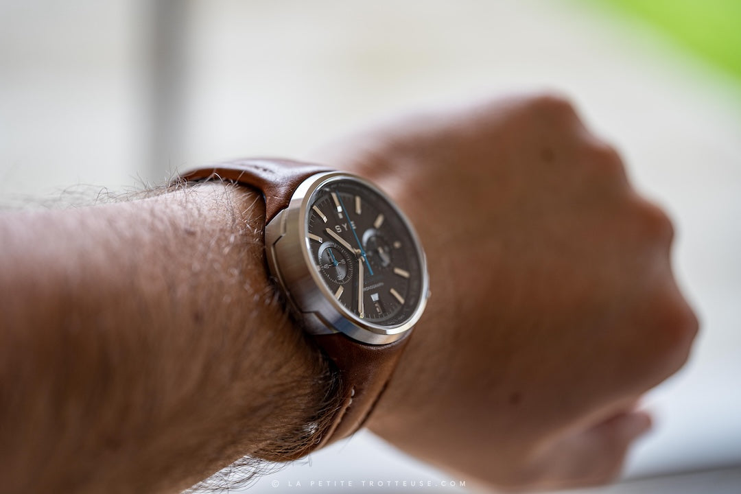 Close-up of a wrist wearing a brown leather watch with a blurred background
