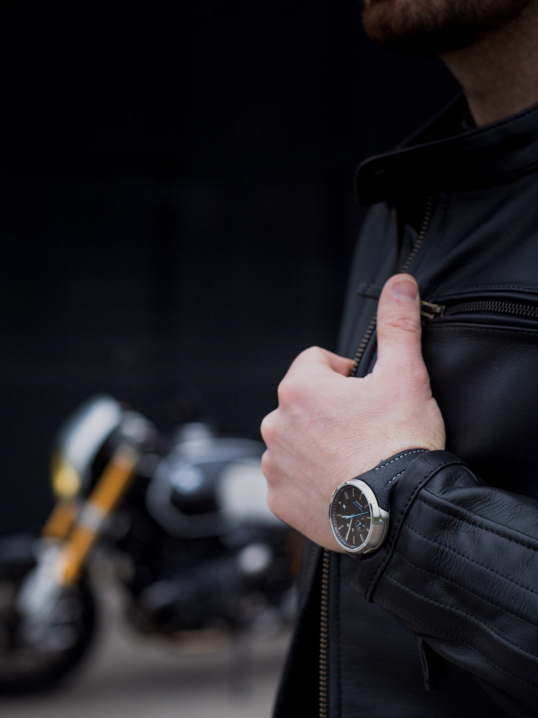 Person wearing a black jacket with a blurred motorcycle in the background