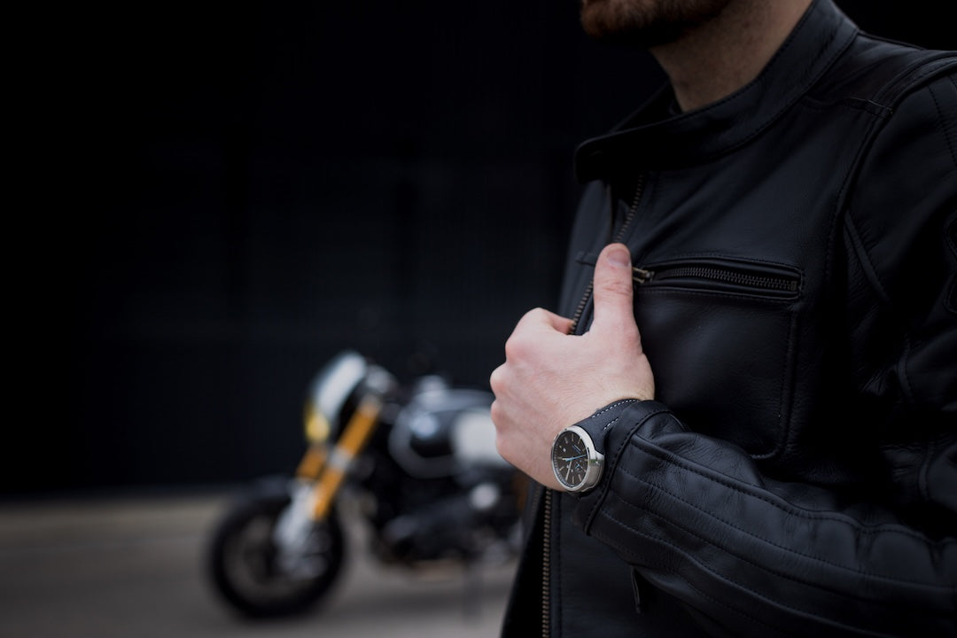 Person wearing a black leather jacket with a motorcycle in the background