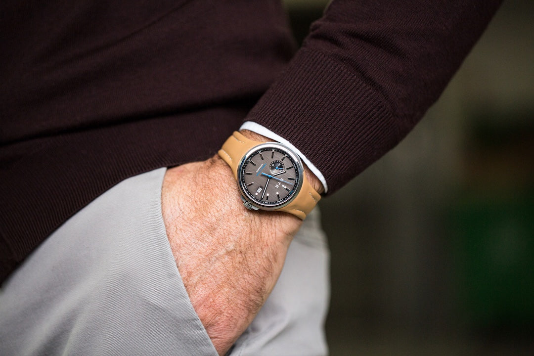 Person wearing a watch with a brown leather strap and dark face, blurred background