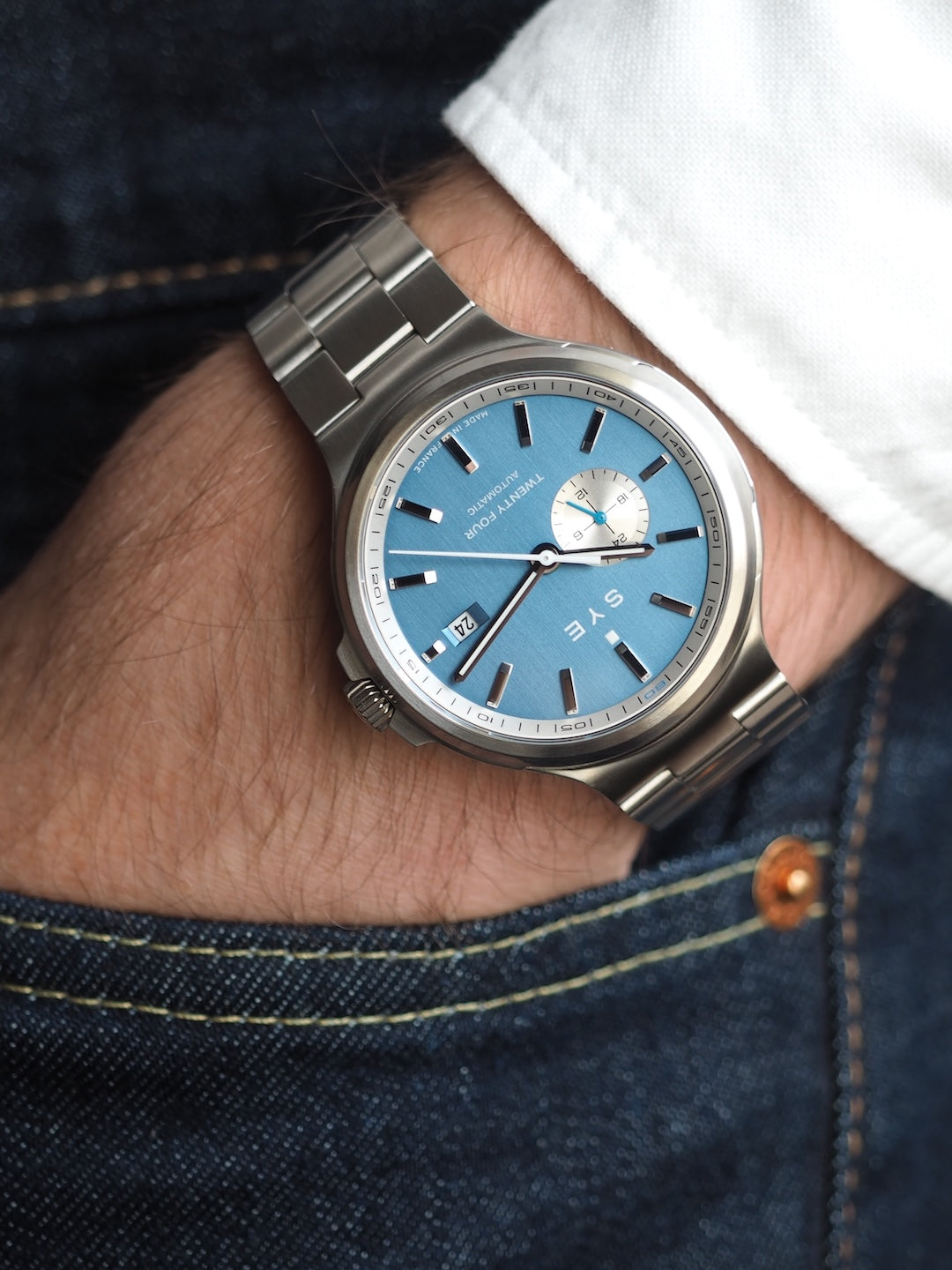 Silver watch with a blue face on a wrist, wearing a denim jacket.