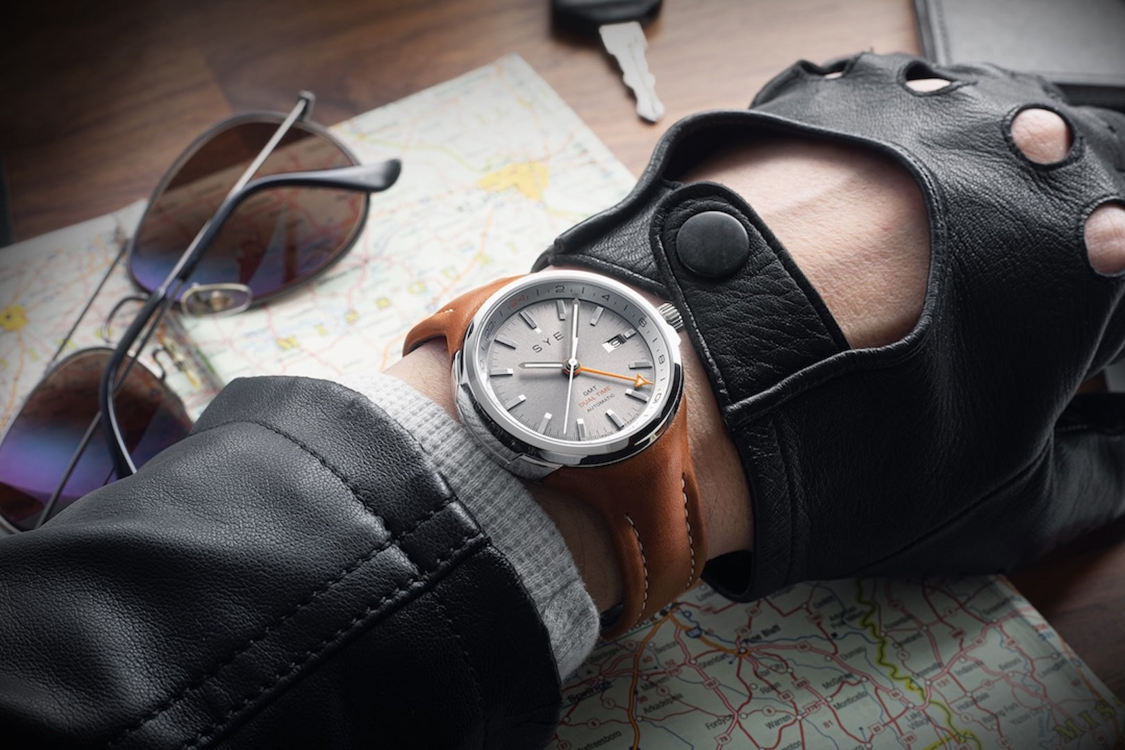Hand wearing a leather glove with a watch, sunglasses, and a map in the background