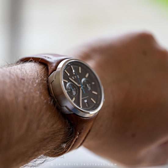 Close-up of a wrist wearing a brown leather watch with a blurred background