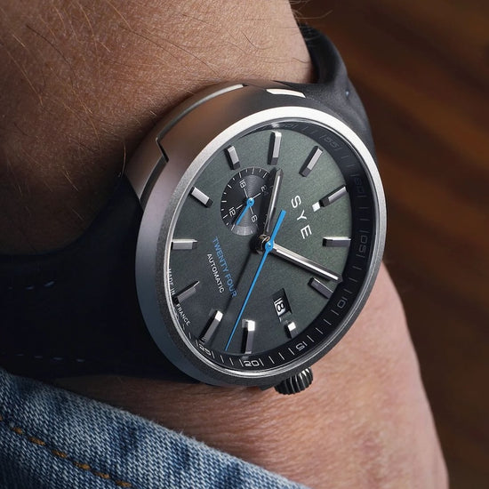 Black SYE watch on a person's wrist with a blurred background