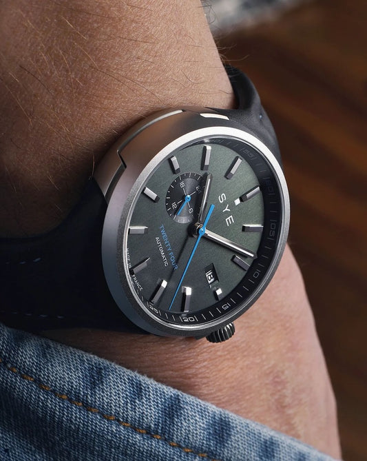 Black SYE watch on a person's wrist with a blurred background