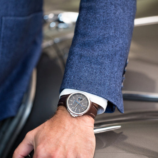 Hand wearing a watch with a blue suit sleeve, sitting on a car seat.