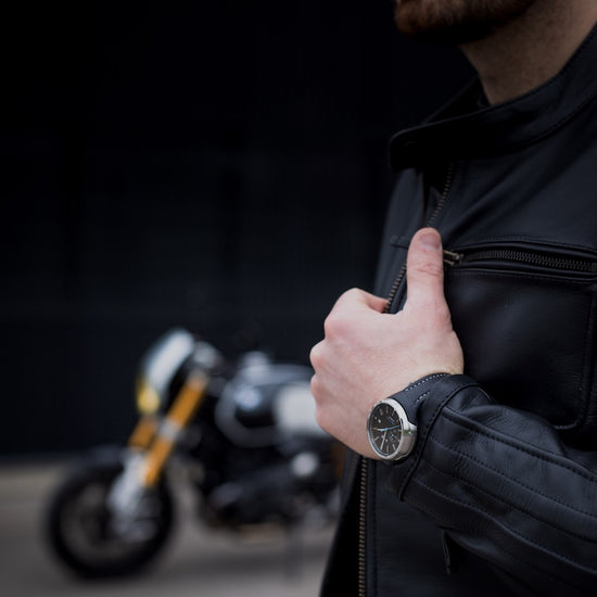 Person wearing a black leather jacket with a motorcycle in the background