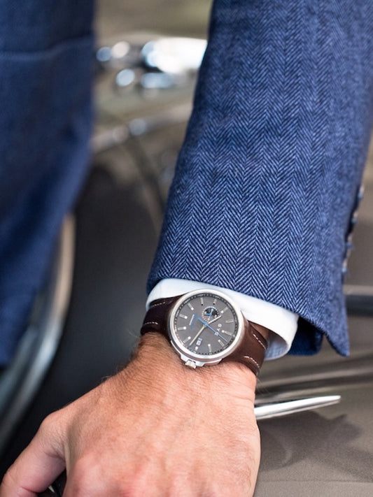 Close-up of a person wearing a watch with a blue suit and car interior in the background
