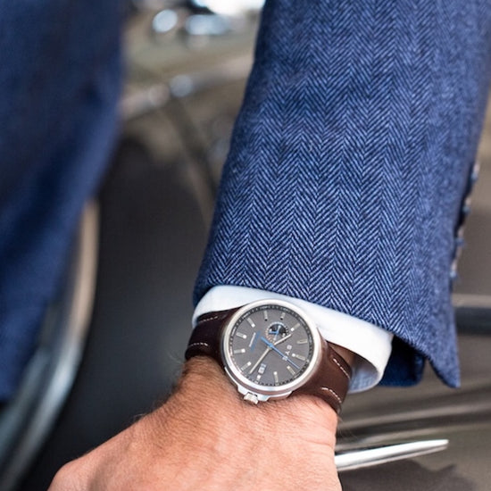 Close-up of a person wearing a watch with a blue suit and car interior in the background
