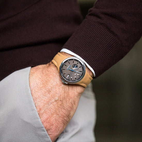 Person wearing a watch with a brown leather strap and dark face, blurred background