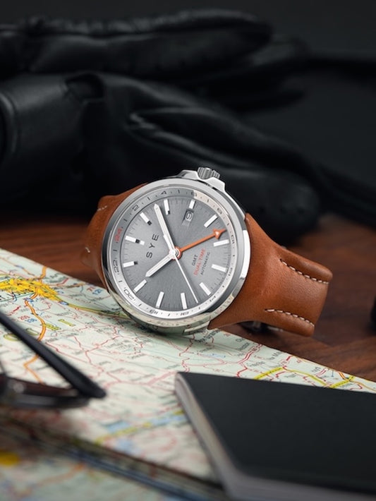 Watch with brown leather strap on a map with gloves and pen in the background