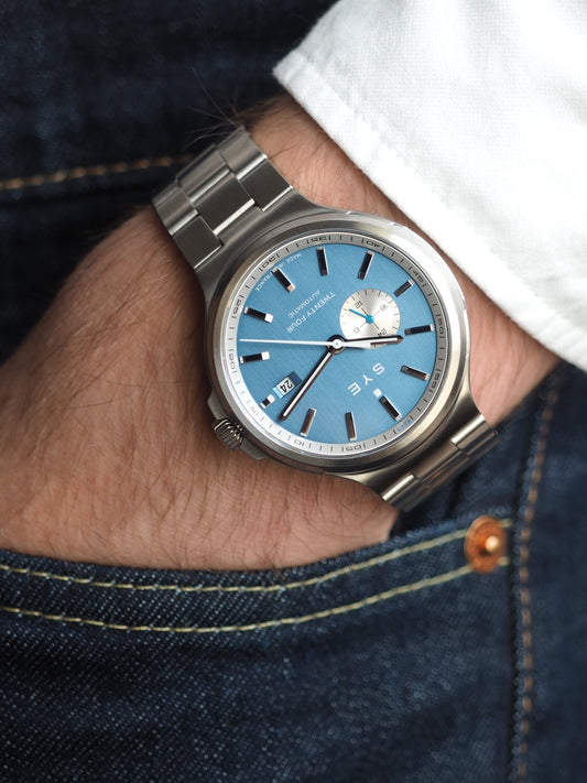 Silver watch with a blue face on a wrist, wearing denim jeans.