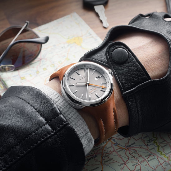 Hand wearing a leather glove with a watch, sunglasses, and a map in the background