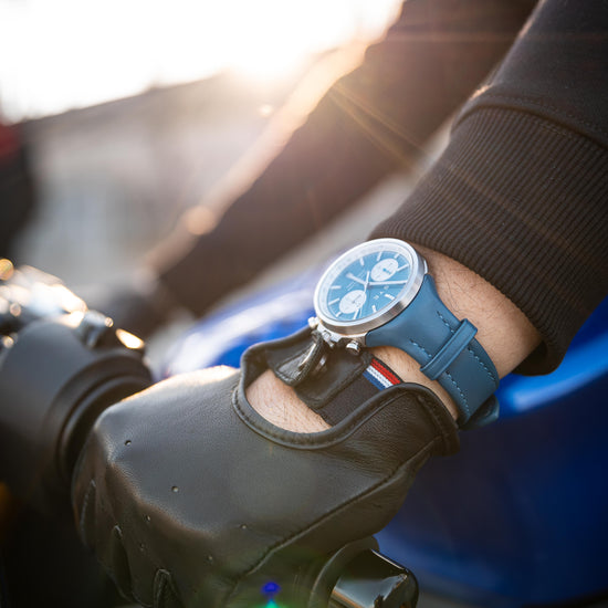 Person wearing a glove and holding a motorcycle handlebar with a watch on the wrist.